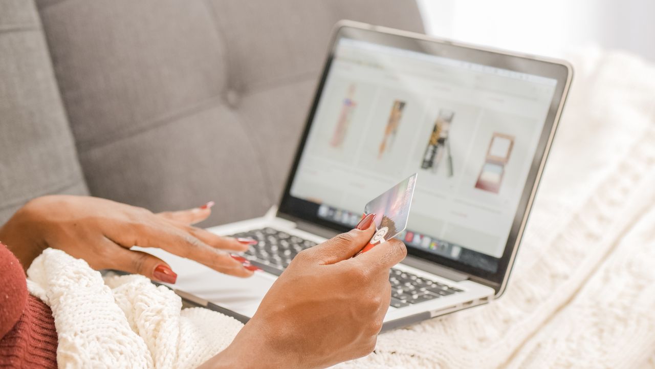about-bg A woman relaxes on a couch while shopping online using her laptop and credit card.